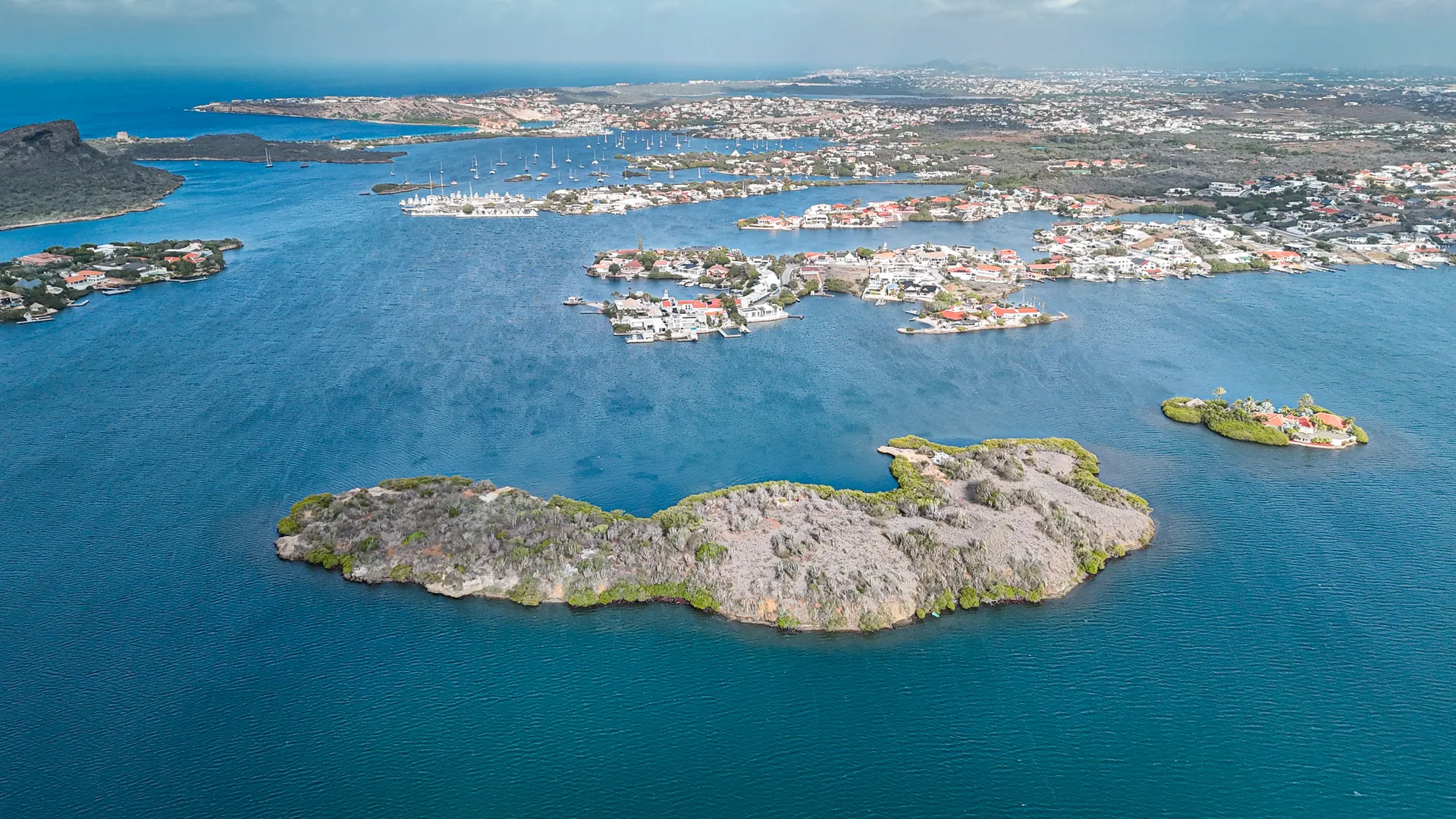 Aerial photograph of Spanish Water, Curaçao, showing the protected inland bay, its residential waterfront and moored yachts beyond Isla di Yerba.