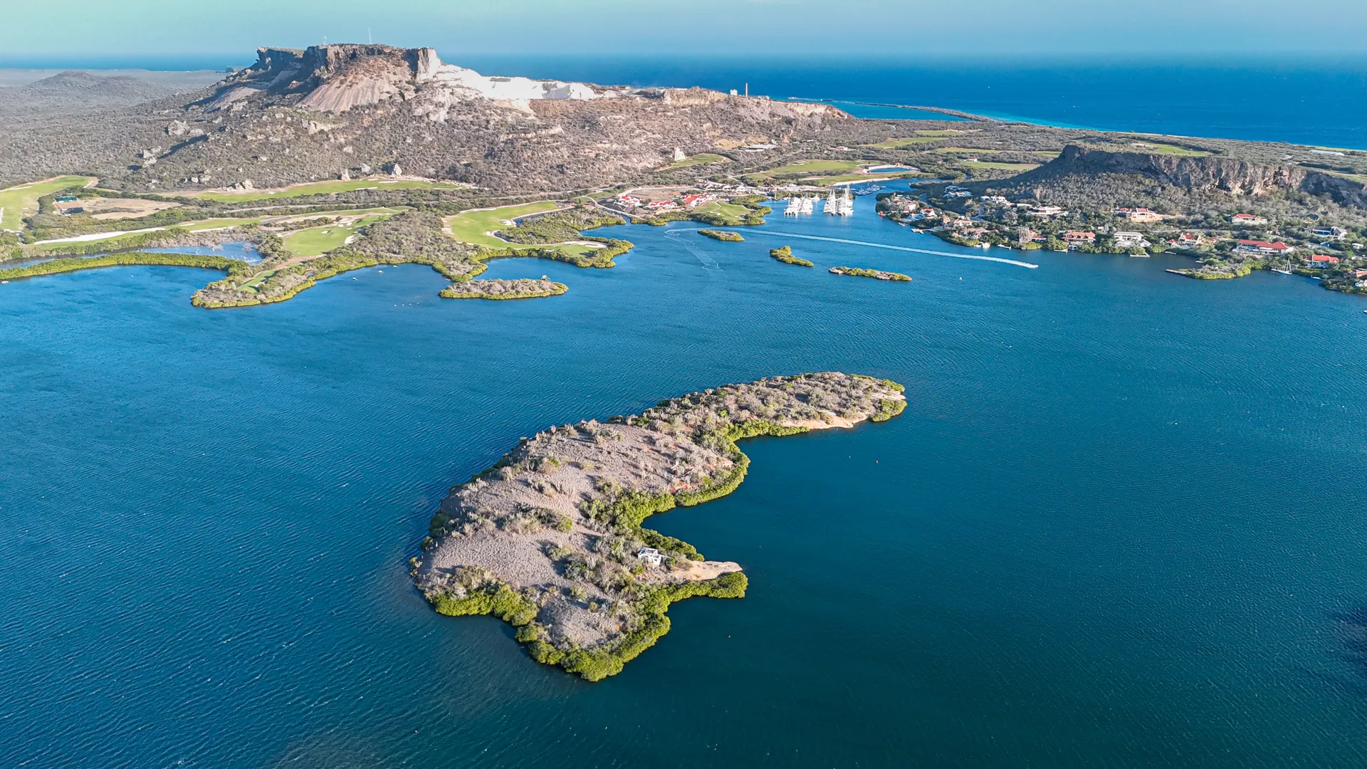 Aerial photograph of Isla di Yerba, a private island in Spanish Water, Curaçao, with the Tafelberg ridge and the open Caribbean beyond.